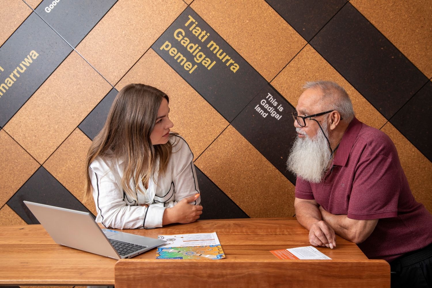 a man and a woman sitting at a desk talking with a laptop in front of them